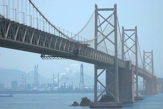 Majestic Seto Ohashi Bridge spanning the blue sea with an industrial factory landscape in the hazy background, Japan.