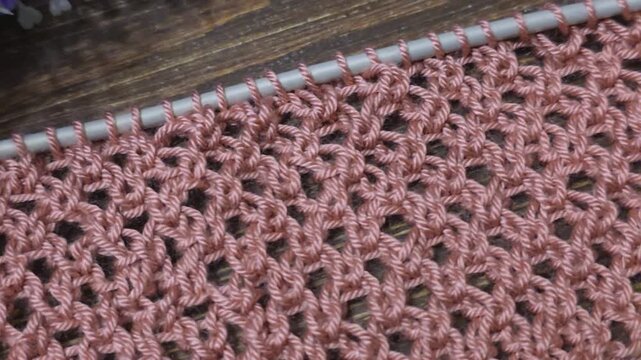 A textured, openwork knitting pattern made with colored yarn on a wooden surface with decorative flowers. Close-up of the knitting texture and pattern. Conceptual ideas for handicrafts