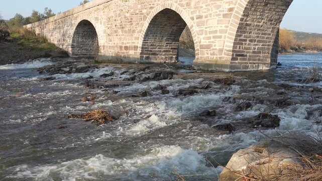 Ancient Stone Bridge over Tuzla Stream near Assos, Behramkale, Turkey Historical Ottoman Architecture and River Landscape at Sunset. High quality 4k footage