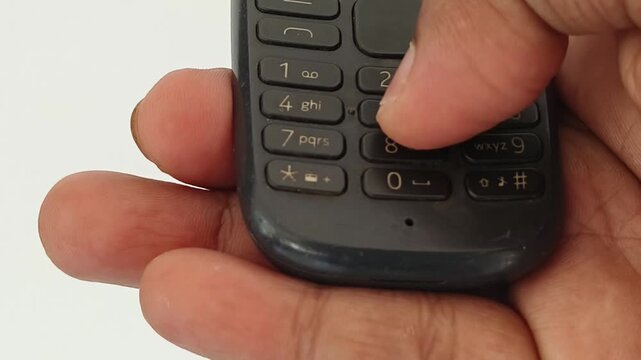 Extreme closeup of hand holding old vintage keypad mobile phone and finger dialling physical number button for calling. Nostalgic 90s technology portable and wireless communication equipment.