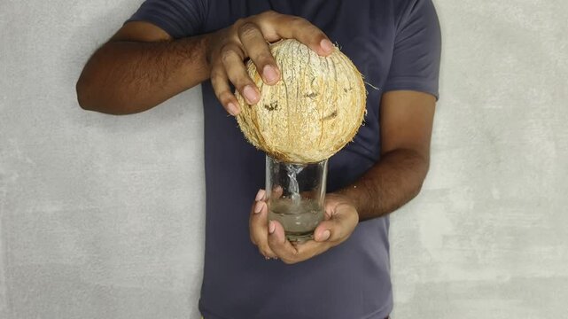 Indian man holding fresh and organic coconut and pouring healthy coco water or juice liquid into glass for drink. Tropical sweet and tasty refreshment beverage with natural vitamin and protein.