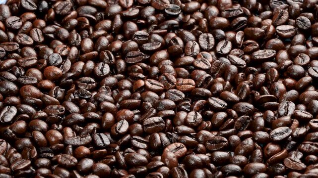 Horizontal rotating macro of dark roasted coffee beans with softbox lighting. Premium glossy texture for cafe and barista cinematic backgrounds.