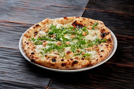 Gourmet white pizza with arugula, cashews, and parmesan cheese on a dark wooden background. Crispy Neapolitan style crust. Professional food shot.