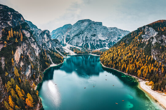 Emerald alpine lake Pragser Wildsee with dolomites mountain, rowboats and autumn pine forest in Lake Braies, Italy