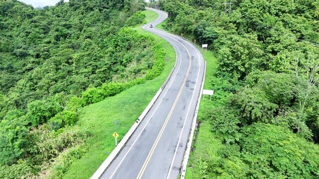 Winding Road Curves Through Lush Green Hills and Dense Forest, Offering Scenic View of Vibrant Vegetation and Picturesque Landscape