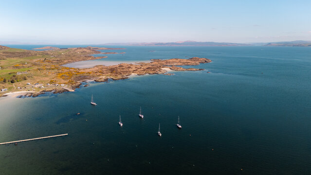 Aerial view of sailboats resting on the water near the white sandy beach and distant islands, Isle of Gigha, Argyll and Bute, Scotland.
