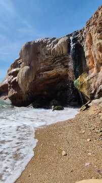 Natural thermal waterfall flowing into the sea at Loutra Edipsou, Evia island, Greece. Hot mineral springs cascading over rocks into the blue Aegean waters, a famous volcanic spa destination.