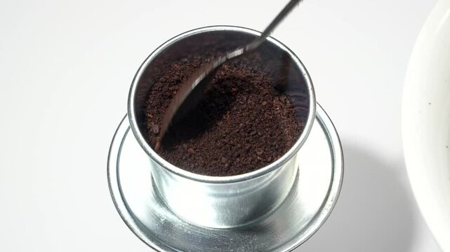 Extreme close up rotating macro of scooping ground coffee into a traditional Vietnamese metal phin filter on a white background. Premium ingredient concept.
