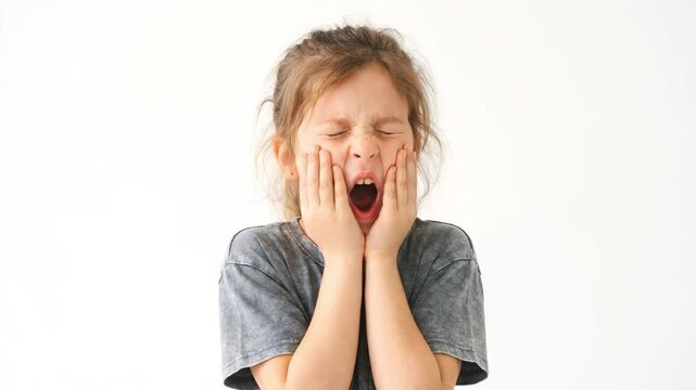 Sleepy little girl yawning with hands on cheeks. Tired caucasian child opening mouth wide on white background. Morning routine and childhood fatigue concept. Copy space