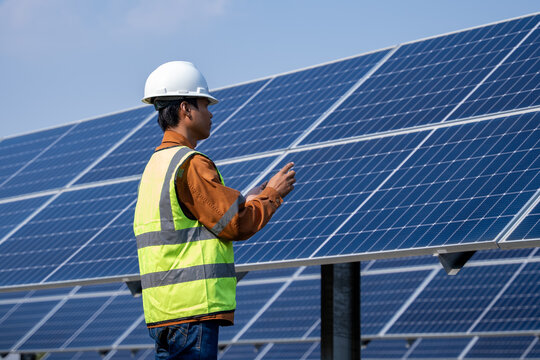 Technician inspect photovoltaic panels in a solar farm, wearing safety gear and monitoring system performance under clear sky conditions, ideal for renewable energy operations and maintenance visuals.