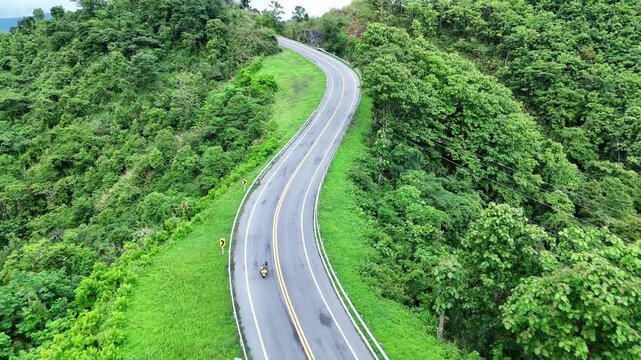 Aerial View of Winding Road Through Lush Green Forest Scenic and Tranquil Journey with Motorcyclist on Curve Amidst Vibrant Greenery
