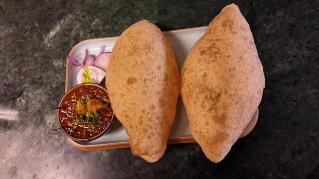 Top view of traditional Indian chole bhature served on a plate with spicy chickpea curry, sliced onions, and pickle. Crispy golden bhature paired with rich, flavorful chole creates a classic North Ind