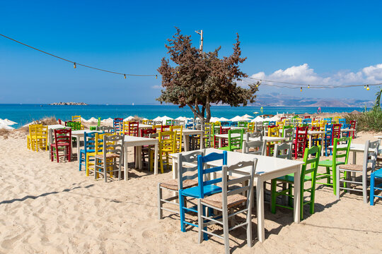 Group of colorful chairs and tables arranged on the sand of a beach during a summer day.
