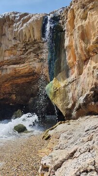 Natural thermal waterfall flowing into the sea at Loutra Edipsou, Evia island, Greece. Hot mineral springs cascading over rocks into the blue Aegean waters, a famous volcanic spa destination.