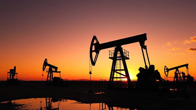 Silhouettes of oil pump jacks at vibrant sunset in oilfield