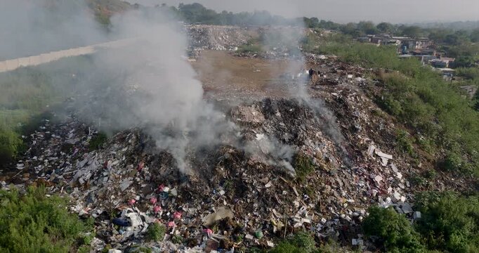 Aerial zoom in view. Burning rubbish causing greenhouse gas, contributor to climate change.  Extreme Poverty. People living alongside dumpsite struggling to survive through waste picking.