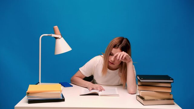 Tired female student falling asleep while studying, reading books for an exam, and feeling bored and sleepy at her desk