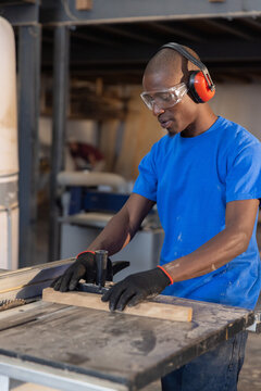 Table saw slicing wooden plank on workshop workbench, showing dust-covered tools and beams overhead