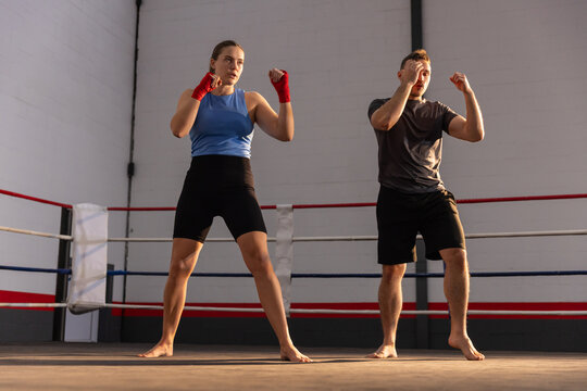 Female and male athletes standing in boxing ring holding guarded stance with red wraps