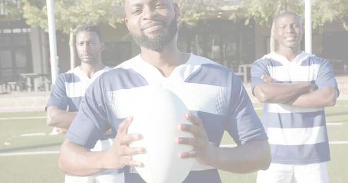 Holding bearded player adjusting grip, smiling on field in striped kit with oval ball and posts