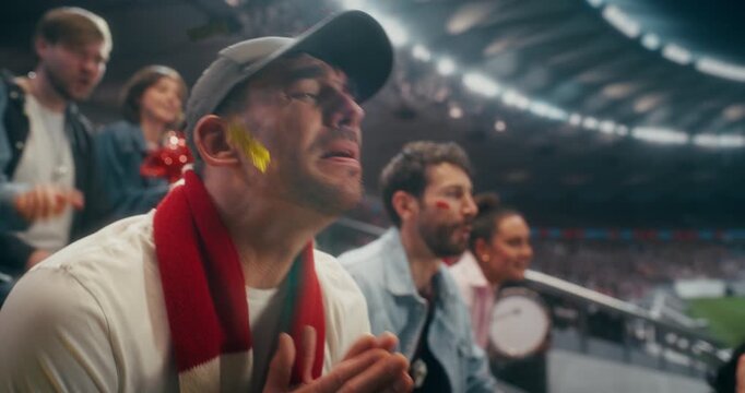 Portrait of a Happy White Male Soccer Fan in Red Scarf Cheering, Smiling and Raising His Arms With Supporters in a Packed Night Stadium During a Professional International League Match, Slow Motion