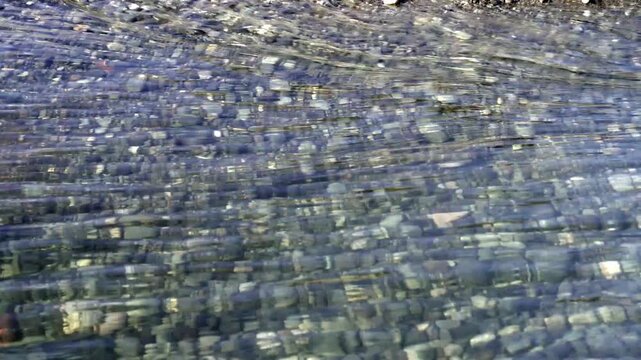 Clear river water flowing over deep gravel bed with sunlight reflections