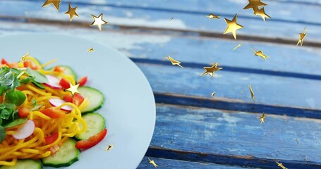 Displaying white ceramic plate with spiral noodles salad on worn blue table, gold stars, copy space © vectorfusionart