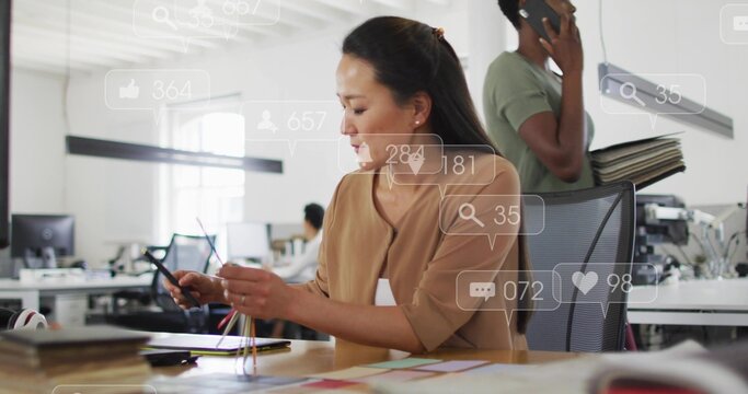 Working mid adult Korean designer in tan blouse handling color strips at open office, with overlays