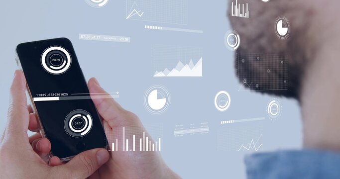 Holding smartphone, bearded man wearing blue collared shirt studying floating HUD graphs at office