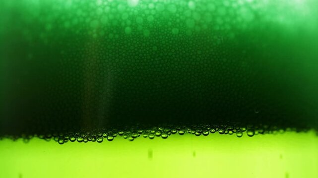 Fresh beer is poured into a glass, lots of bubbles and foam with a macro view, green glass