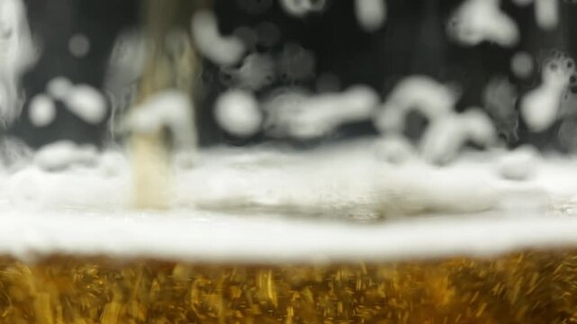 Fresh beer is poured into a glass, lots of foam and bubbles, close up view