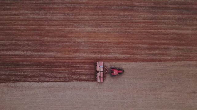 Tractor pulling disc harrow performing soil tillage in Formosa, Goi&aacute;s, Central-West Brazil, creating worked strip and visible contrast with uncultivated soil, top down follow drone shot.