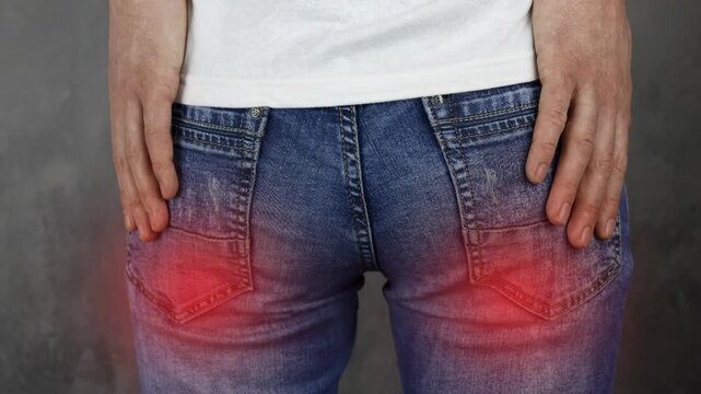 Close-up of a man grabbing his painful buttocks due to hemorrhoids, prostatitis, or sciatica
