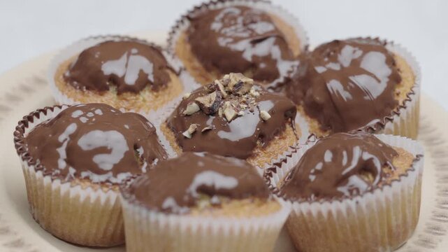 Hand adds chopped nuts on chocolate glazed muffins in close up dessert preparation