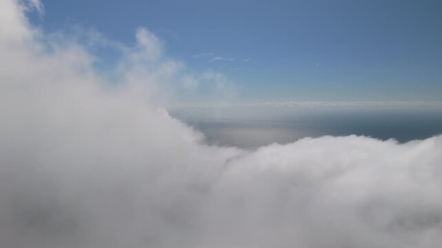 Exciting 4K drone clip diving directly through a thick cloud layer over the ocean. Emerging from the mist to reveal a stunning sunny sea horizon under a clear blue sky. Smooth transition.