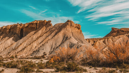 Naklejka premium Steep cliff in arid mountainous semi desert landscape with vegetation under a blue sky with some thin clouds. Desierto de Tabernas, Almeria, Andalusia, Spain.