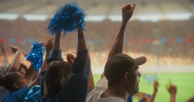 Rear view Diverse Crowd of Soccer Supporters Celebrating in a Packed stadium With a White Woman and a Man in a Cap Raising Their Arms During a Professional League and World Tournament Match.