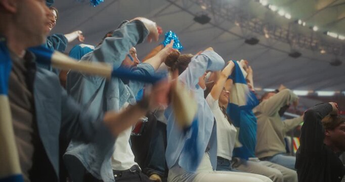 Male and Female Soccer Supporters Leap, Shout and Lift Blue Scarves in a Packed Championship stadium Celebrating a Decisive Match Moment as the Roaring Crowd Dances Under Bright Arena Lights.