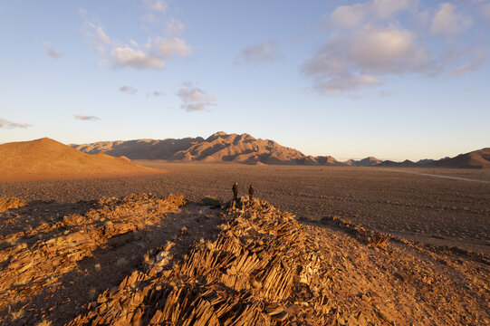 Aerial view of the rugged, sun-kissed Namib Desert landscape under a pastel sky, where rocky ridges meet the vast horizon, Windhoek, Namibia.