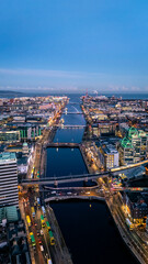 Fototapeta premium Portrait shot looking down river Liffey in Dublin at blue hour dawn night time with illuminated cityscape buildings and clear blue sky in winter