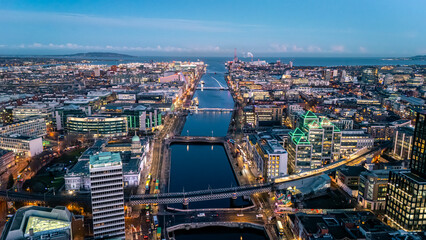 landscape shot looking down river Liffey in Dublin at blue hour dawn night time with illuminated cityscape buildings and clear blue sky in winter © STJMEDIA