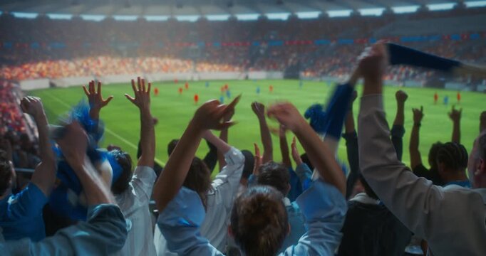 Back-view Soccer Supporters Erupt in Celebration Inside a Packed Stadium, Waving Blue and White Scarves, Clapping and Raising hands as a Professional International Championship Match Unfolds Field