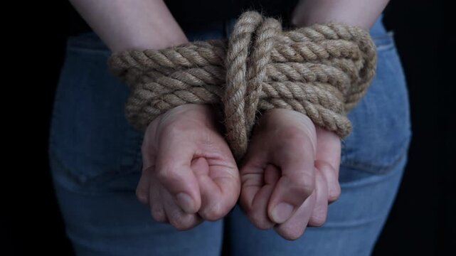 Helpless woman with her hands tied behind her back showing her struggle against a black background