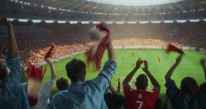 Back View of Diverse Soccer Supporters Celebrating in a Packed Stadium, Waving Scarves and Victory Props, Clapping and Raising Arms During a Professional International Championship Match