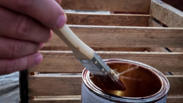 Hand Holding Brush Dipping Into Wood Stain for Crate Restoration