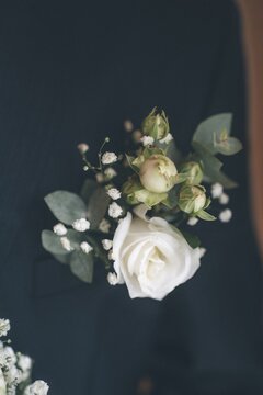 A man in a gray jacket and white shirt. It has a black bowtie on it. In the jacket pocket there is a bouquet of white flowers with green leaves.
