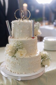 Elegant wedding cake with rings and white flowers, held by newlyweds in celebration