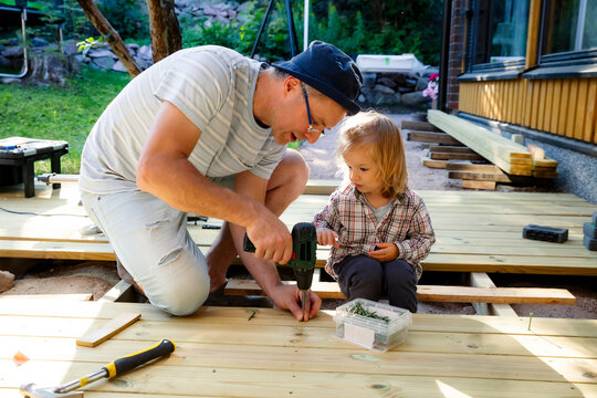 Joyful father and little child building a wooden patio deck together. Authentic family DIY home improvement project, sunny outdoor leisure.