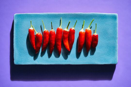 Vibrant still life of a row of red chili peppers on a turquoise blue plate
