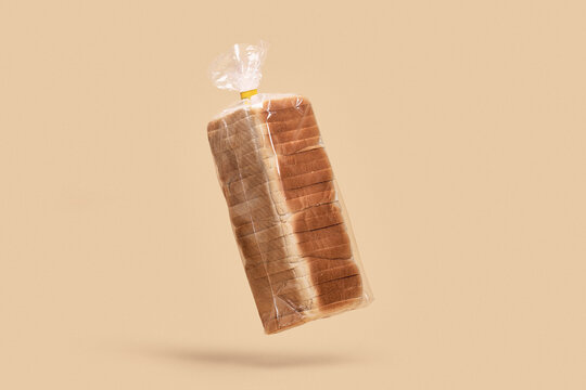 Loaf of sliced bread in clear plastic bag floating against peach background
